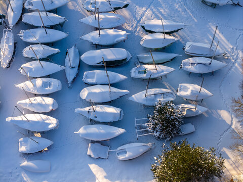Aerial view of rows of sailboats covered in thick white snow with long shadows on a sunny winter day in Trakai, Vilnius County, Lithuania.
