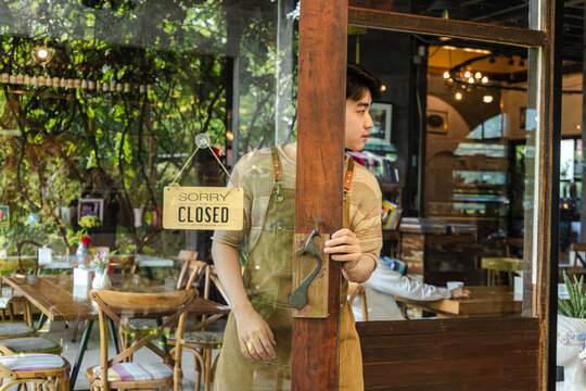 Young barista cafe owner smiling at entrance with open sign visible, confident entrepreneur representing hospitality service and customer readiness, positive mood in small business operation.