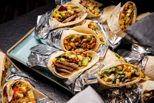 Assorted beef and vegetable wraps wrapped in aluminum foil on a blue platter