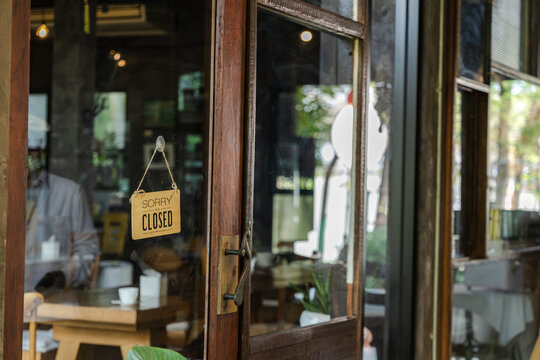 Young barista small business cafe owner interacting with customer at entrance while closed sign visible representing business limitation or timing control in coffee shop, new generation entrepreneur
