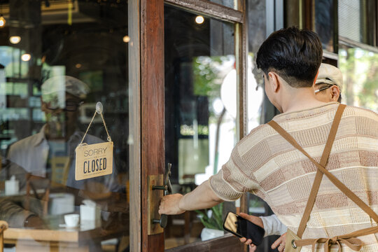 Young barista small business cafe owner interacting with customer at entrance while closed sign visible representing business limitation or timing control in coffee shop, new generation entrepreneur