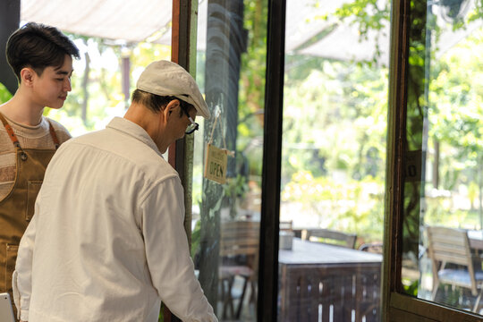 Young small business cafe owner barista open sign welcome gesture standing at entrance inviting customers into coffee shop friendly service concept and positive business presentation, cheerful worker