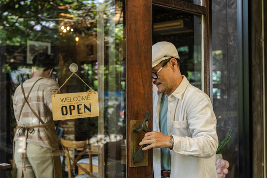 Family small business, senior cafe owner placing hiring sign on glass door, recruitment and expanding team concept in local coffee shop and restaurant. Cafe owner teaching barista about work process