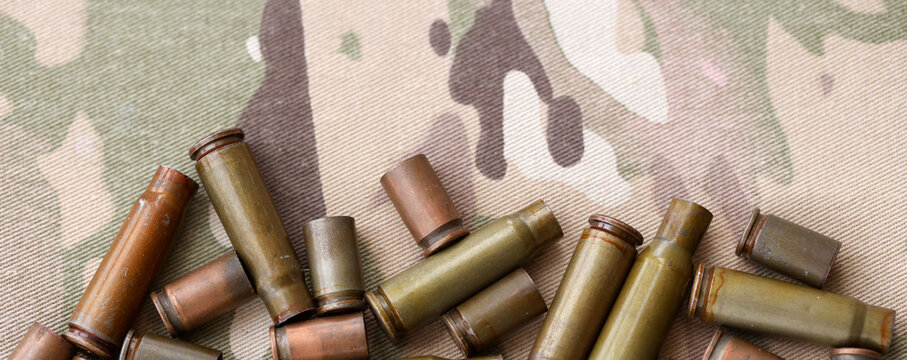 Big amount of shells cartridges from assault rifle bullets on old camouflage fabric.
