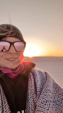 Selfie video of a happy woman tourist spinning around at sunset in Salar de Uyuni, smiling traveler enjoying freedom in Bolivia salt flats desert wearing traditional pattern poncho and sunglasses