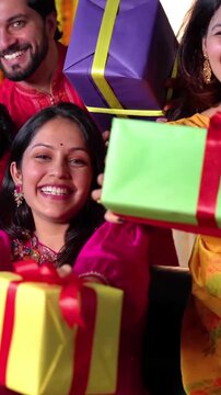  A happy Indian family of four in festive mood and attire expressing joy and happiness with gifts in their hands celebrating Diwali in their brightly decorated home with indoor plants, little lights