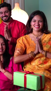 A joyful Indian family of four in traditional  attire smiles together, exchange gifts and warm wishes during a heartwarming Diwali celebration in their well decorated home.