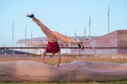 Female athlete performing a dynamic handstand with wide leg split on a stone sculpture in an urban outdoor park setting