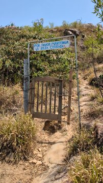 Rustic wooden gate on a dirt hiking trail with a Spanish sign reading por favor mantenga la reja cerrada, leading up a sunny mountain path, ideal for travel, adventure, and trekking concepts
