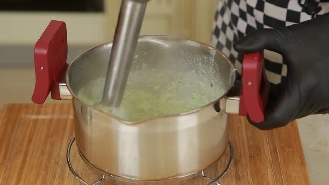 Chef using blender to puree boiled broccoli in a pot while preparing a broccoli cream soup