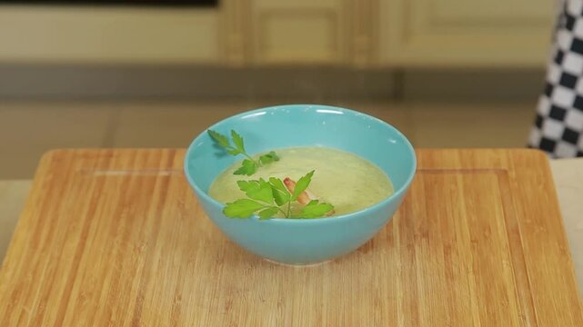 A chef plating and presenting broccoli cream soup with shrimp and fresh herbs