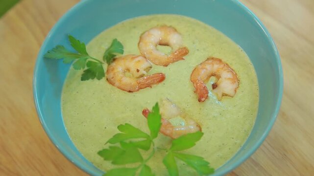 Presenting broccoli cream soup with shrimp and fresh herbs