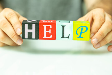Hands hold and spell out HELP with alphabet blocks, signifying assistance or support. © vegefox.com