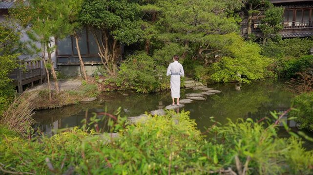 Man in yukata walking on stepping stones in Japanese garden