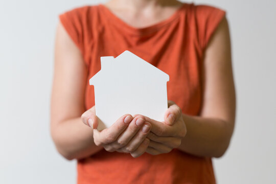 Person's hands cradle a small white house shape representing home ownership