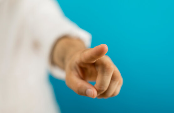 Hand pointing towards camera on blue background, representing choice, action, and direction.