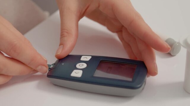 A woman uses her hands to insert a test strip into a glucometer. This action is part of checking blood sugar levels for diabetes management.