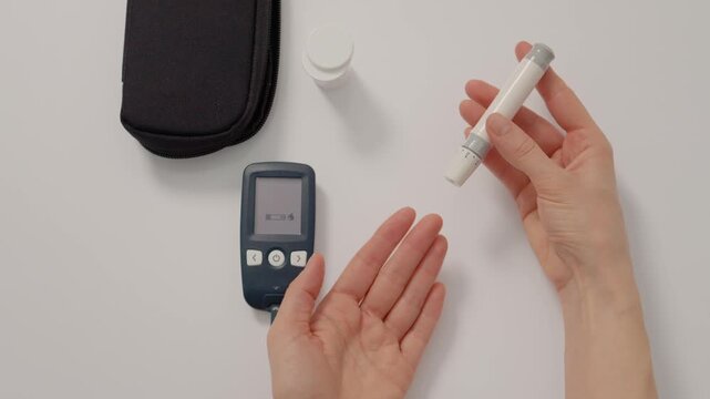 A woman holds a finger pricking device to measure her blood sugar levels at home. She prepares to check her glucose for health monitoring.