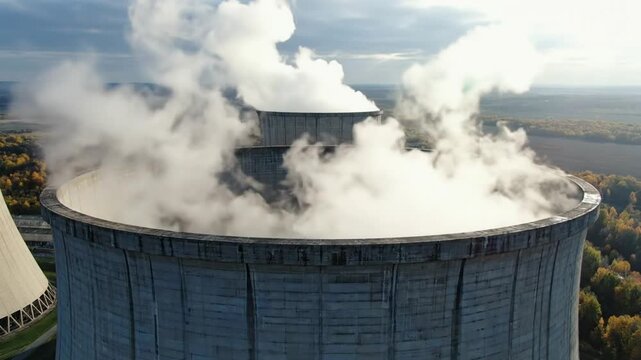 Industrial nuclear power plant cooling tower emitting steam with bright cloudy sky aerial view