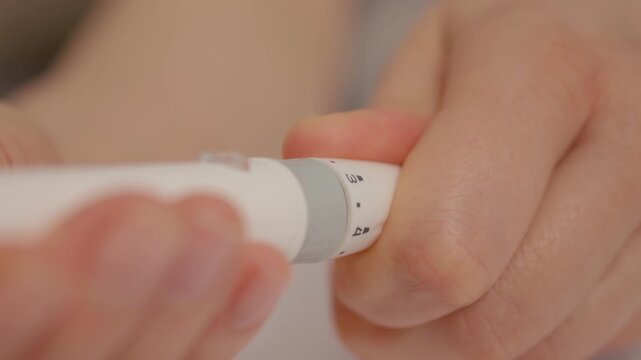 A woman prepares to test her blood sugar levels using a finger pricking device. She is focused on the process to monitor her glucose levels.