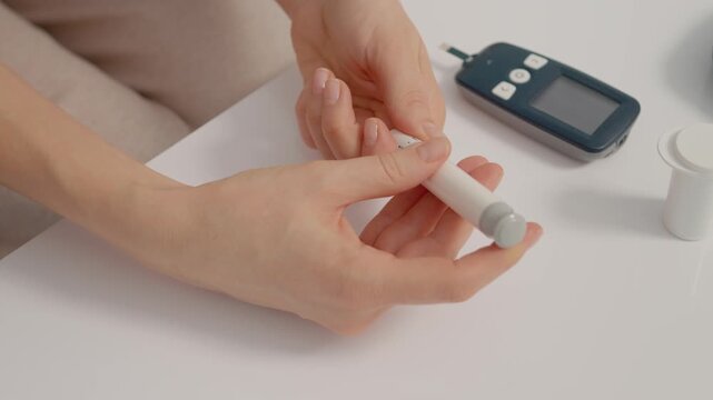 A woman prepares to check her blood sugar levels using a finger pricking device and a glucometer on a table. She focuses on her task and measures glucose.