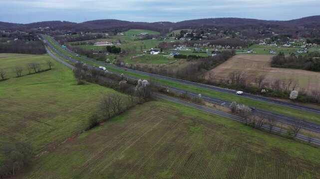 Multilane rural span along US15 near Elmer Derr Rd with traffic movement, open farmland, scattered farmsteads stretching toward low ridges west of Frederick highlights varied crops, Maryland