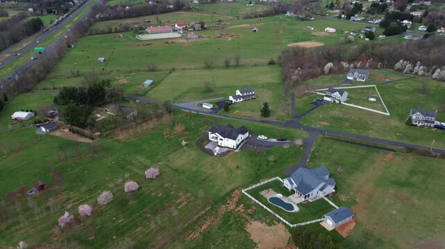 Highway agricultural sweep along US15 near Elmer Derr Rd with broad fields, flowering tree clusters, scattered buildings marking rural edge west of Frederick, mixed soil textures, Maryland
