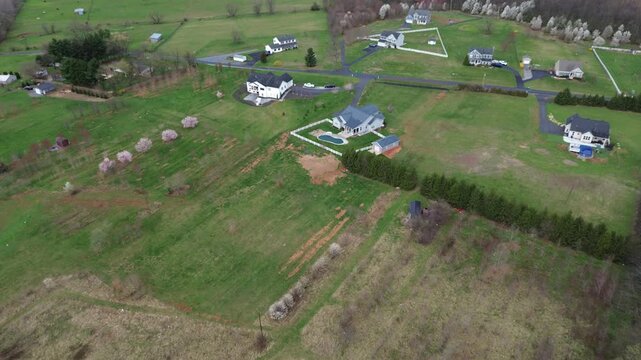 Residential farmland transition near Elmer Derr Rd with spaced homes, fenced yards, open fields extending toward US15 along western Frederick landscape shows bright lawn, blooming trees, Maryland