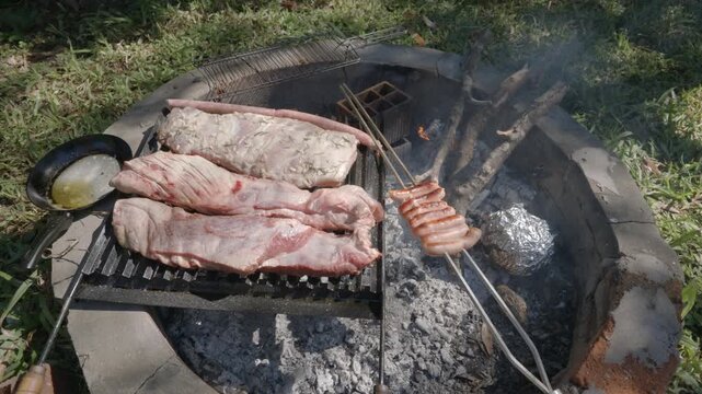 A traditional barbecue setup with skewered sausages and marinated ribs grilling over a charcoal pit. Ideal for culinary content or cultural documentaries.
