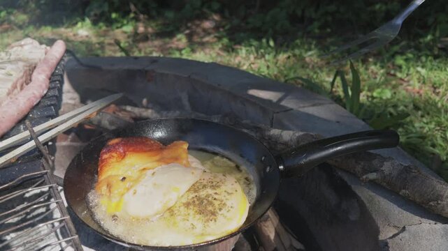 Close-up of hands grilling Argentine provoleta cheese over an open fire. Ideal for culinary blogs or barbecue-themed content.