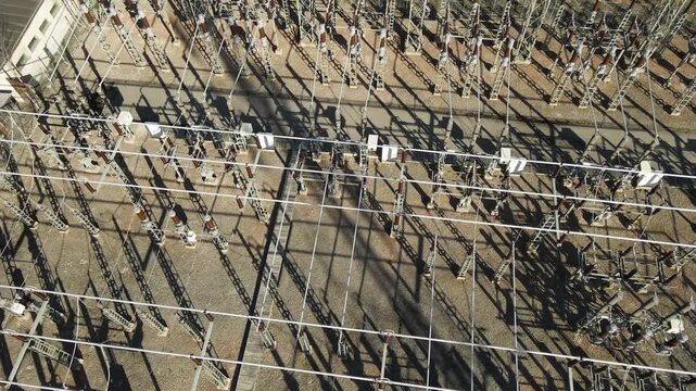 High voltage electrical substation with a complex network of power lines, transformers, and switchgears generating and distributing electricity to the urban area on a sunny day with long shadows