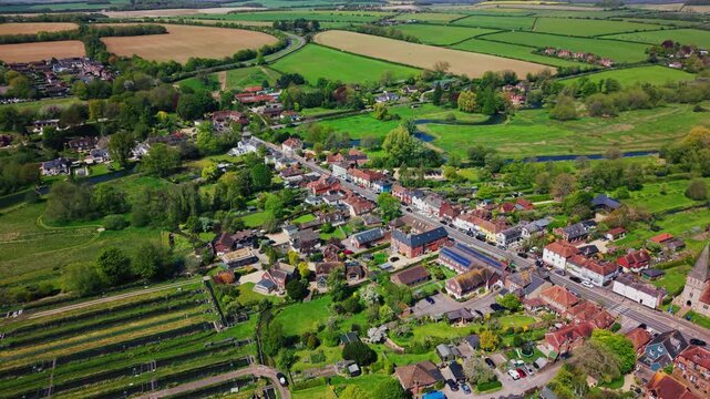 Drone aerial view over Stockbridge village in Hampshire, England, showing the high street, rooftops, green countryside, fields and rural landscape in spring.