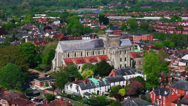Close aerial drone view of Romsey Abbey surrounded by houses, rooftops and trees in the historic town of Romsey, Hampshire, England.