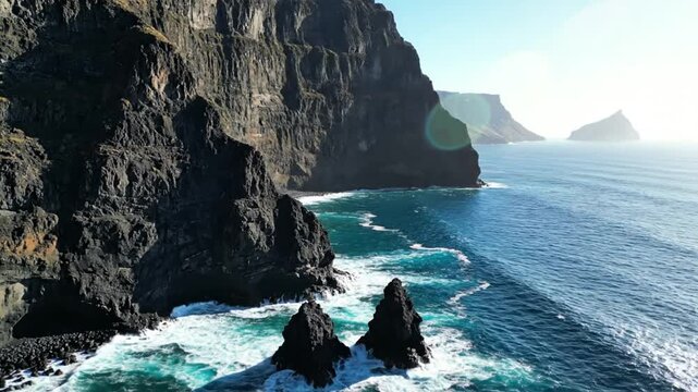 Epic aerial view of a dramatic rocky coastline with sea stacks and ocean waves under a sunny sky