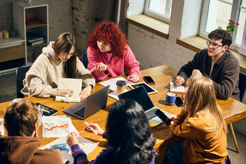 Obraz premium Young people collaborating around wooden table with laptops and charts. Concept of business planning, creative agency work, student workshop, teamwork, analytics, and office training.