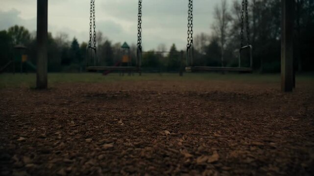 Gloomy Empty Playground Swings Stand Still Under Overcast Sky Daytime Outdoor Scene With Wood Chips Ground and Distant Trees