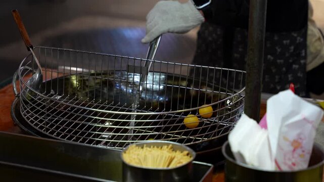 Taiwanese street food vendor deep frying sweet potato balls in a wok at a bustling night market