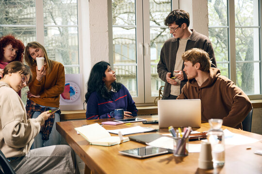 Office workers discussing project strategy around table in creative workspace. Concept of team briefing, agency workflow, business planning, corporate coaching, and collaborative office culture.