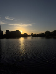 Obraz premium Sunset over water with silhouettes of buildings and trees in the evening sky of golden hours