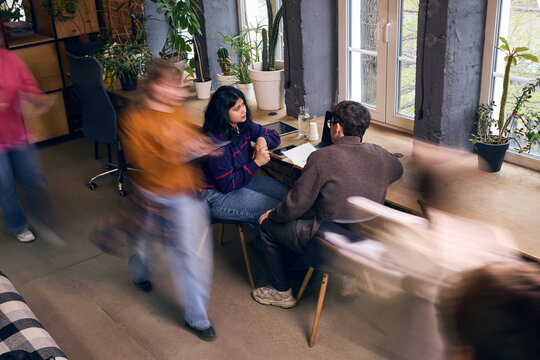 Busy creative office with motion blur around focused business discussion. Concept of fast workflow, team pressure, startup management, coworking energy, and modern business communication.