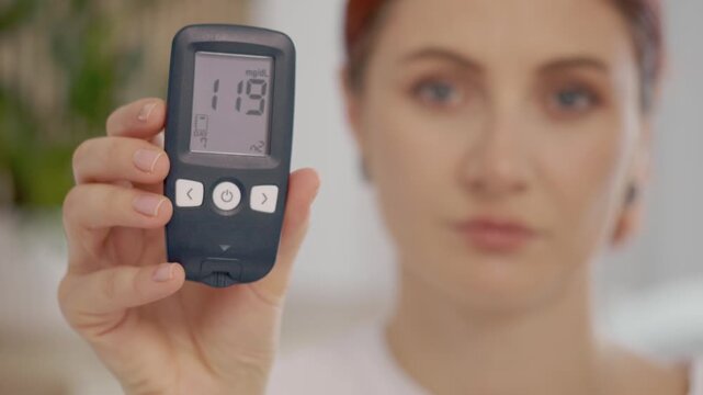 A woman holds a glucometer showing a reading of 119 mg dL while discussing blood sugar levels. This moment emphasizes the importance of monitoring glucose health.