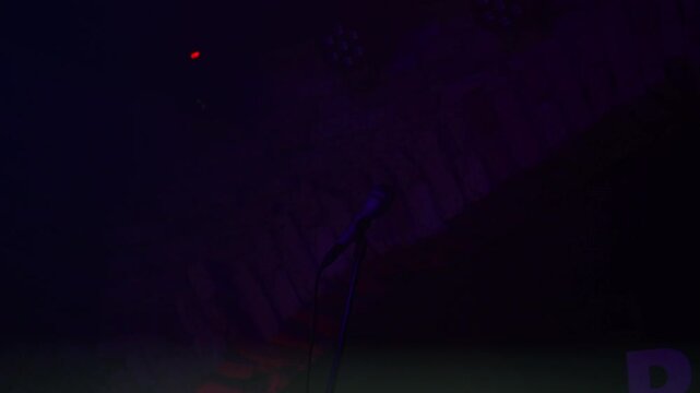 Professional microphone on stand for open mic or karaoke night show on empty stage. Dark club interior with spotlights and haze before live music performance or stand up comedy event night.