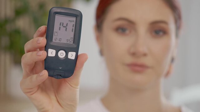A woman holds up a glucometer showing a reading of 141 mg dL, indicating a high blood sugar level. She shares her concern about diabetes management.