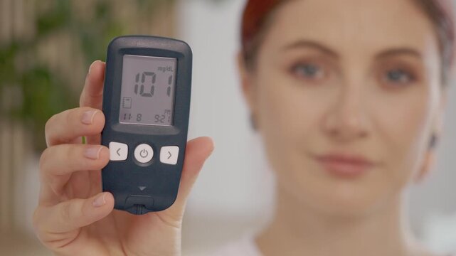 A woman shows her glucometer reading of 101 mg dL. This reading is near the limit for healthy and diabetic blood sugar levels. Understanding this is important for health.