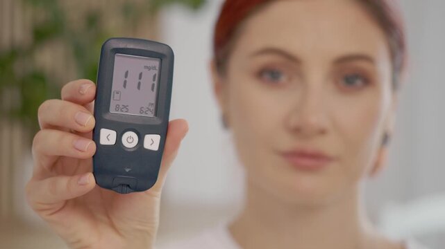 A woman holds a glucometer up to the camera that shows a reading of 111 mg dL. This is an important moment for those monitoring blood sugar levels at home.