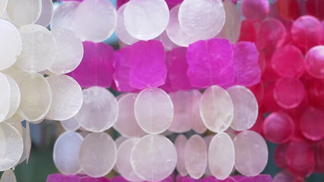Translucent capiz shell hanging decorations swaying gently in the wind, relaxing pastel pink and white abstract motion background with luxury wellness spa ambience and soft dreamy ambient light