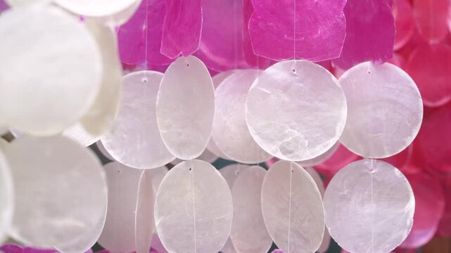 Calm movement of translucent capiz shell hanging decoration swaying in the wind in pink and white pastel tones, abstract luxury interior background with soft light texture, relaxing wellness spa 