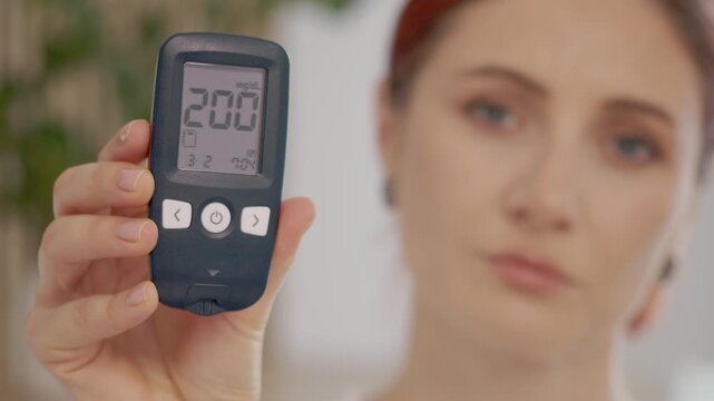 Woman holds a glucometer displaying a blood sugar level of 200 mg dL. This reading indicates a high level of glucose in her blood.