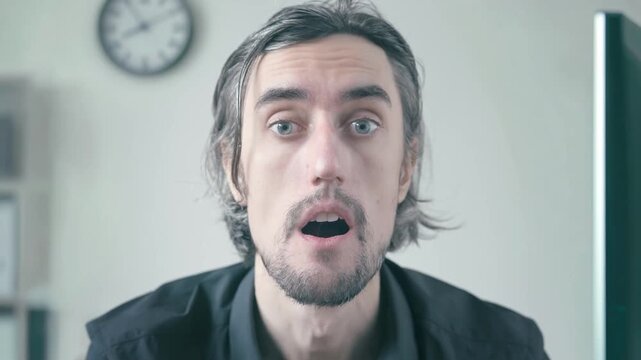 Bored office worker at workplace sitting indoors at his desk in a softly lit office, showing changing facial expressions from mild surprise to astonishment and slight confusion during work