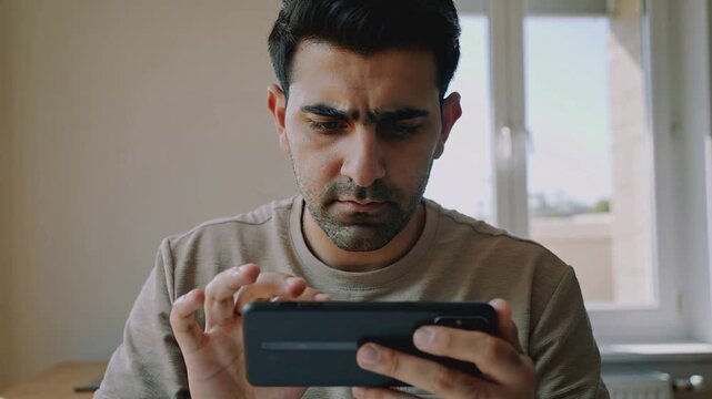 close up of a focused man using a smartphone in landscape mode indoors with a serious expression